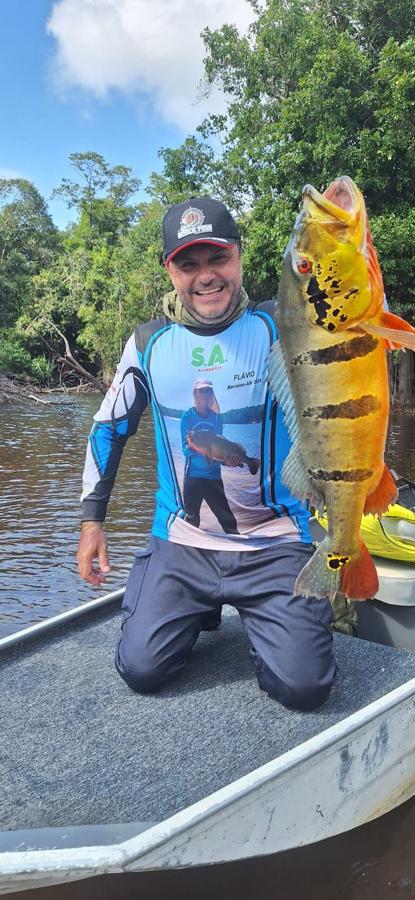 Angler with a colorful peacock bass under blue Amazon skies
