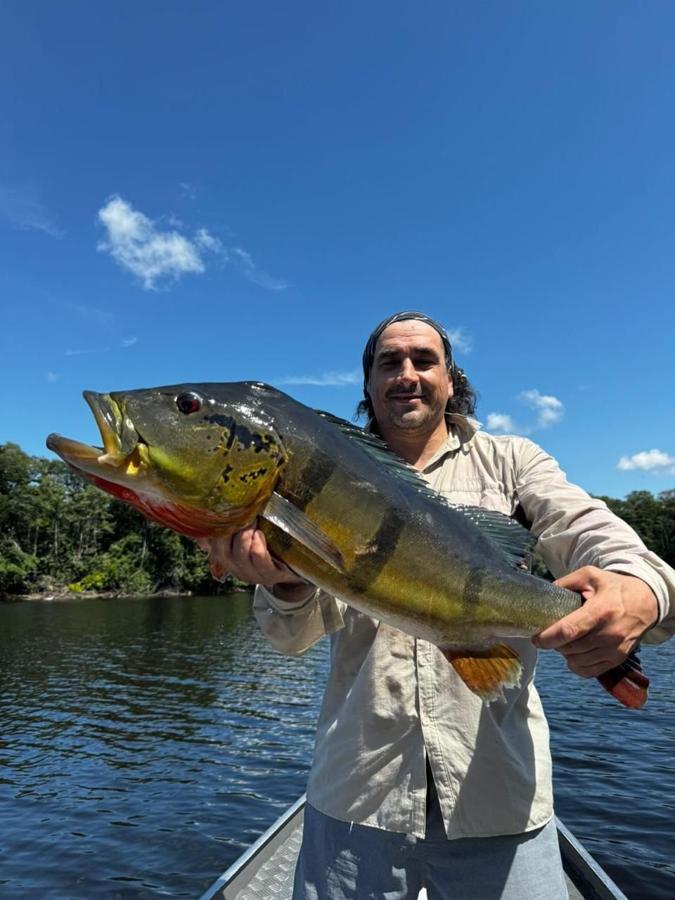 Angler holding a big peacock bass with trees and sky behind