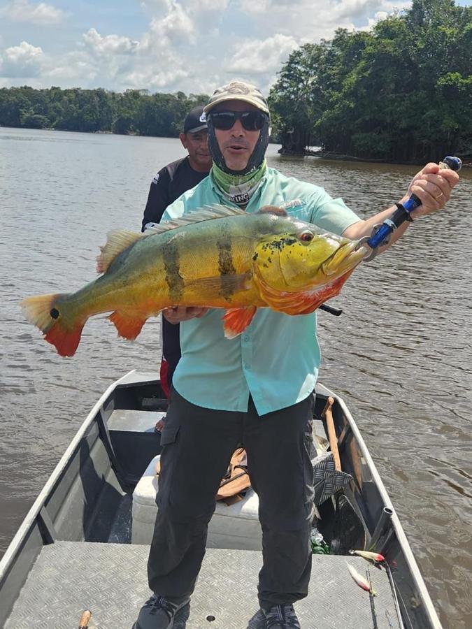 Striped tucunaré held by an angler with guide behind