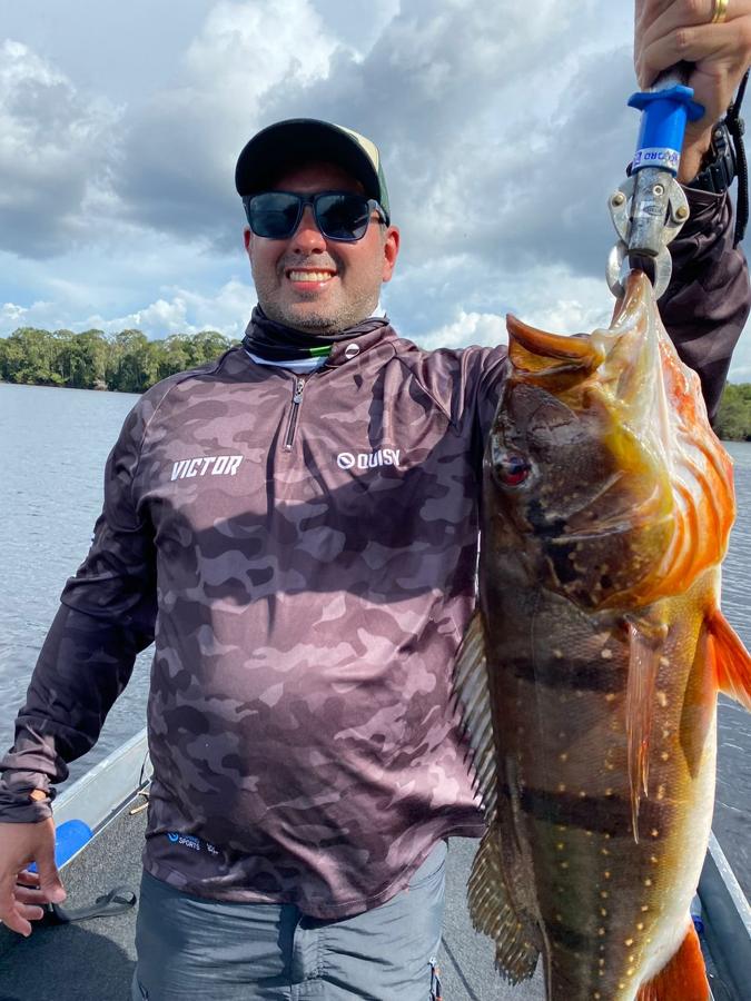 Peacock bass held up against the Rio Negro shoreline
